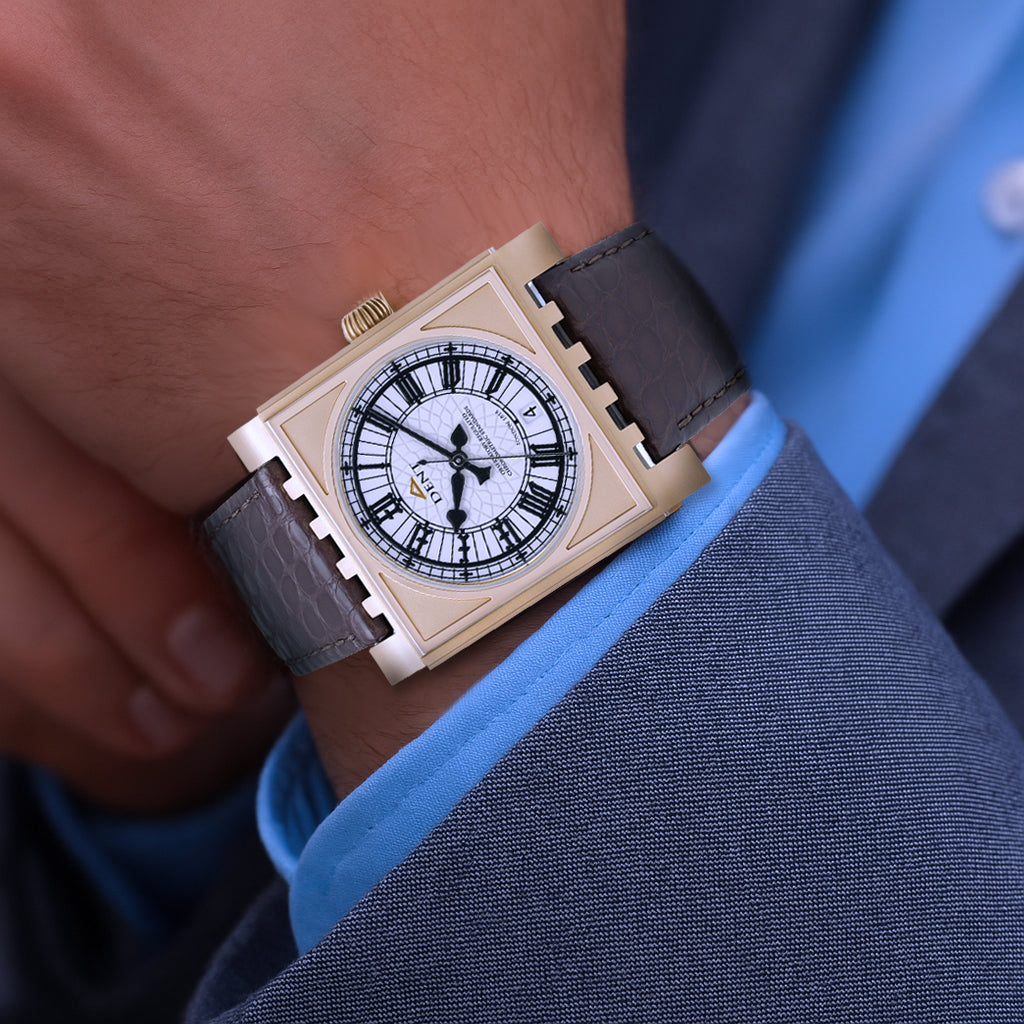 Close-up of a person wearing a gold Dent Parliament watch with a brown leather strap on a blue shirt.